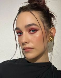 a woman with red eye makeup and gold hoop earrings on her head, looking at the camera