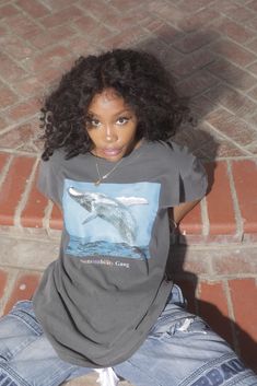 a woman sitting on the ground with her legs crossed and wearing a t - shirt that has an image of a dolphin on it