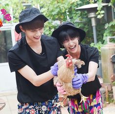 two women in black shirts and purple gloves hold a chicken while smiling at the camera