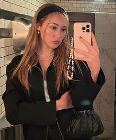 a woman taking a selfie with her cell phone in a public restroom, wearing headbands