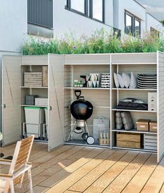 an outdoor storage unit with plants on the top and shelves below, in front of a building