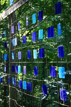 blue glass tiles are hung on a fence in front of some trees and bushes with green leaves