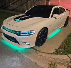 a white dodge charger with green lights on the hood parked in front of a house