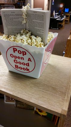 an open book is sitting on top of a bowl of popcorn