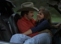 a man and woman sitting in the back seat of a car, one is wearing a cowboy hat