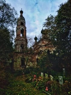 an old church in the middle of some trees and bushes with flowers growing around it