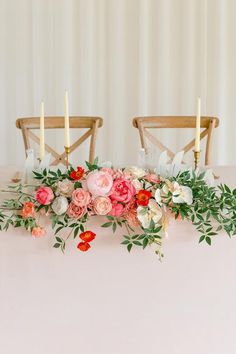 the table is set with candles and flowers on it, along with two wooden chairs