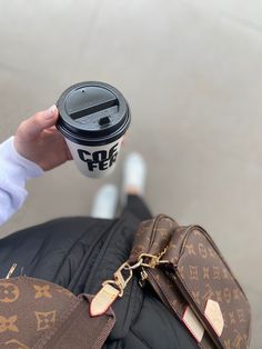 a person holding a coffee cup in their right hand while sitting on the ground next to a purse