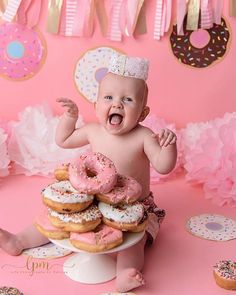 a baby is sitting in front of a pile of doughnuts and wearing a tiara