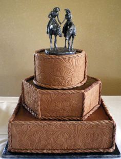 a three tiered cake with two figurines sitting on top of each other