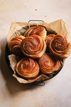 a bunch of cinnamon rolls in a basket on a table top with wax paper around them