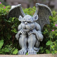 a statue of a gargoyle sitting on top of a rock in front of some bushes