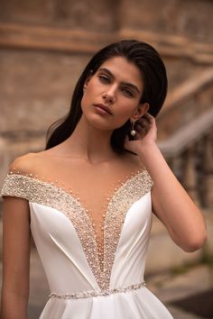 a woman in a white dress posing for the camera with her hand on her shoulder