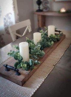 some candles are sitting on top of a wooden tray with greenery in front of it