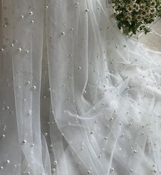 a bouquet of white flowers sitting on top of a bed next to a sheer curtain