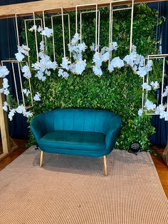 a blue couch sitting in front of a green wall with white flowers hanging from it