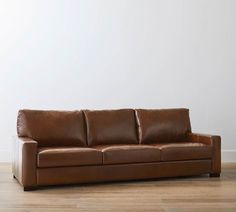 a brown leather couch sitting on top of a hard wood floor next to a white wall