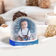 a snow globe with a baby in it sitting on a white blanket next to candles