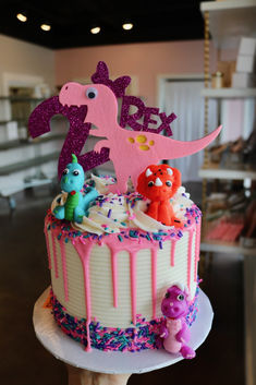 a birthday cake with pink frosting and sprinkles is decorated like a dinosaur