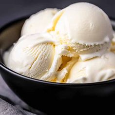 three scoops of vanilla ice cream in a black bowl on a gray tablecloth