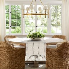 a dining room with wicker chairs and a round table in front of large windows