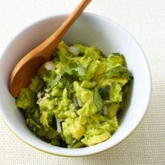 a white bowl filled with guacamole on top of a table next to a wooden spoon