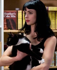 a woman holding a black and white cat in front of a book shelf filled with books