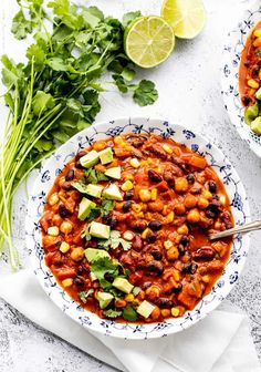 two bowls filled with chili, beans and avocado garnished with cilantro