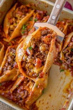 a casserole dish with meat and sauce in it, being lifted by a spatula