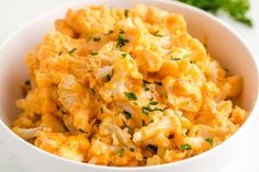 a white bowl filled with macaroni and cheese on top of a table next to parsley