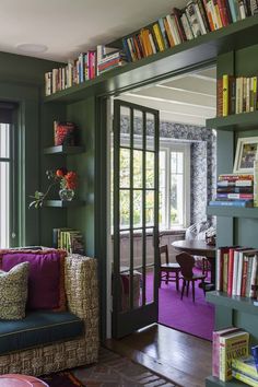 a living room filled with lots of books on top of green walls and wooden floors