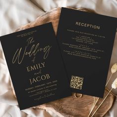 two black and gold wedding cards on top of a wooden tray with dried flowers next to it