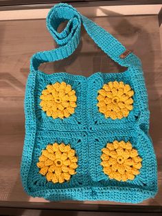 a blue crocheted bag with yellow flowers on the front and bottom, sitting on a table