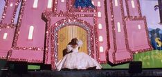 a woman in a white dress standing on top of a stage with a giant pink castle behind her