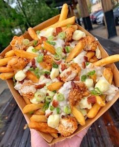 a person holding up a box filled with french fries covered in cheese and toppings