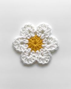 a crocheted white flower with yellow center sitting on top of a white surface