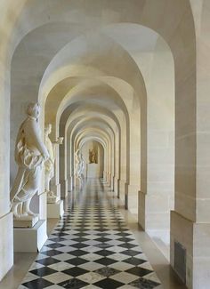 the hallway is lined with marble statues and black and white checkerboard flooring