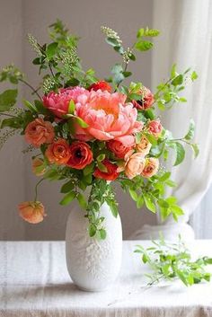 a white vase filled with lots of pink and orange flowers on top of a table