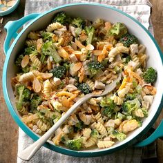 a bowl filled with pasta and broccoli on top of a table next to a spoon