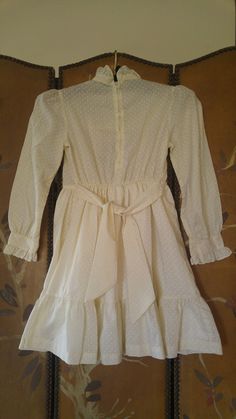 "70's Ivory and white polka dot print dress with hand smocked front and cream lace edging. Ties at sides. Long sleeves with frilly cuffs. High frilly collar. Zip up the back. Dress has underskirt Made by Polly Flinders Size 8 Hand smocked arm to arm across 14\" / bust 28, waist 23\", length 28\"" White Ruffled Prairie Dress For Spring, White Prairie Dress With Ruffles For Spring, Cream Prairie Dress With Ruffles In Cottagecore Style, Cream Cottagecore Prairie Dress With Ruffles, Cream Vintage Dress With Ruffles For Spring, White Long Sleeve Prairie Dress With Ruffles, Vintage Swiss Dot Dress For Spring, Vintage Cream Prairie Dress With Ruffles, Vintage Swiss Dot Dresses For Spring