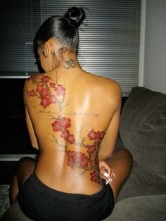 a woman sitting on top of a couch with tattoos on her back and arms behind her