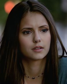 a close up of a person wearing a necklace and looking at the camera with a serious look on her face