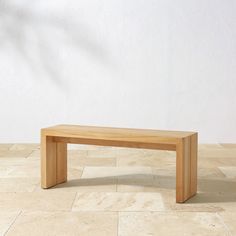 a wooden bench sitting on top of a stone floor next to a planter and wall