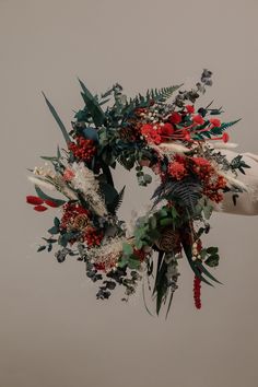 an arrangement of flowers and greenery is hanging from a hook on a wall in front of a gray background