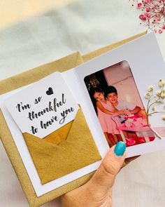 a person holding an open photo book with a message on it and flowers in the background