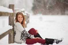 a woman sitting in the snow next to a fence