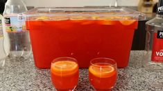 two glasses filled with orange juice sitting on top of a counter next to an ice chest