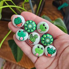 a person is holding six green and white rocks with cactus designs on them in front of a potted plant