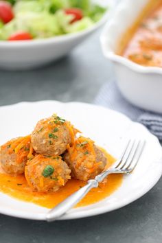 a white plate topped with meatballs covered in gravy next to a bowl of salad