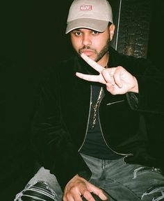 a man sitting down with his fingers in the air and making a peace sign while wearing a hat